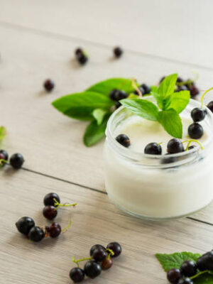 Homemade sweet yogurt in a jar with black currants, on a wooden table .