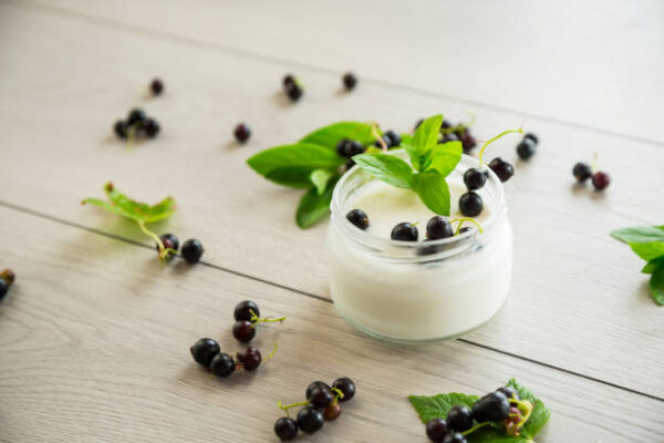 Homemade sweet yogurt in a jar with black currants, on a wooden table .